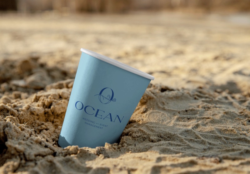 Ocean event branding on a blue cup in the sand